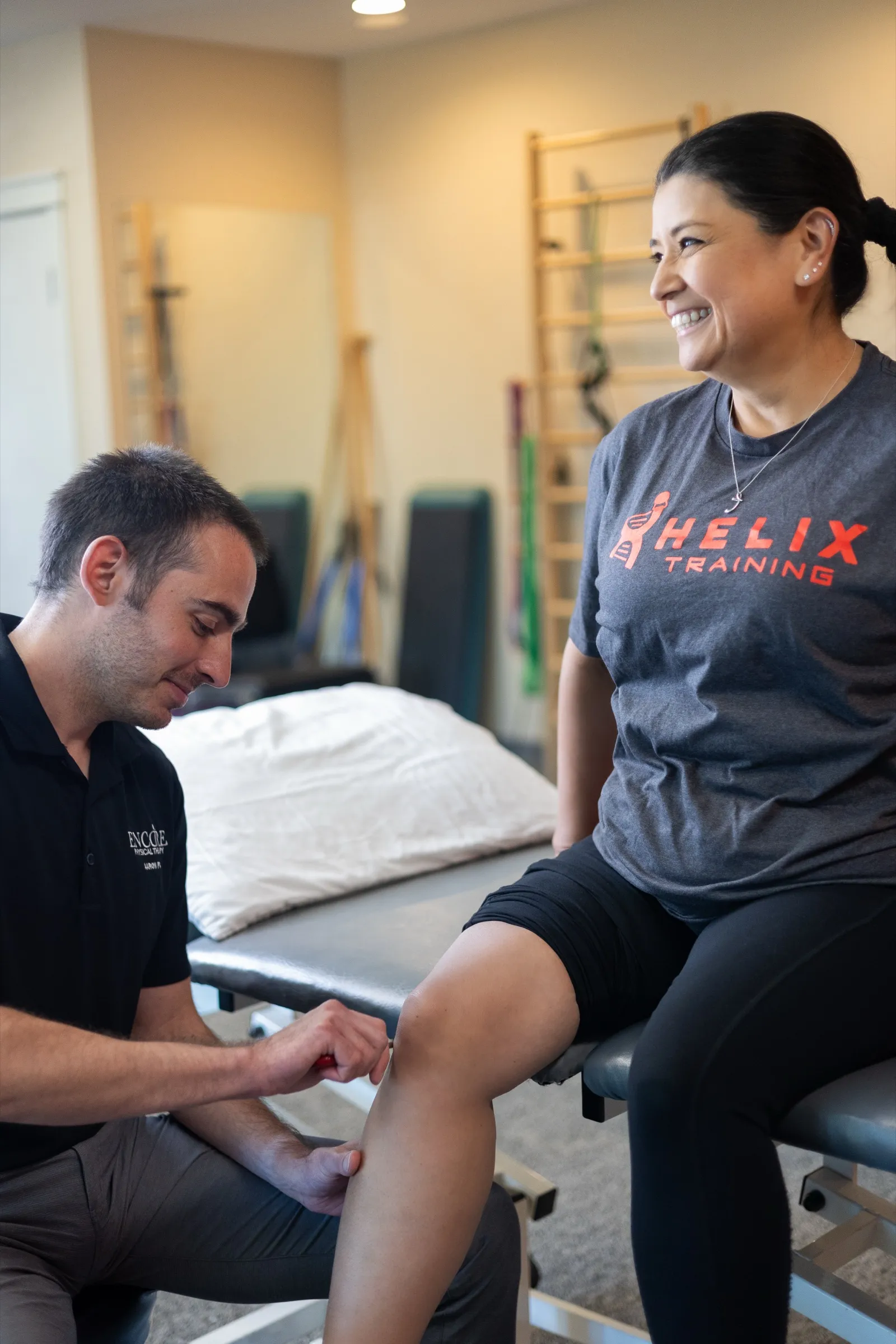 An Encore therapist evaluating the knee of a smiling patient on a treatment table