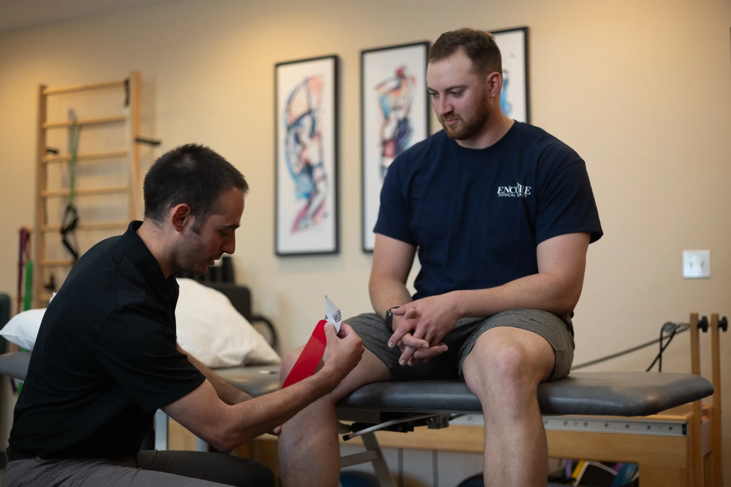 An Encore physical therapist taping the knee of a seated patient in the treatment room
