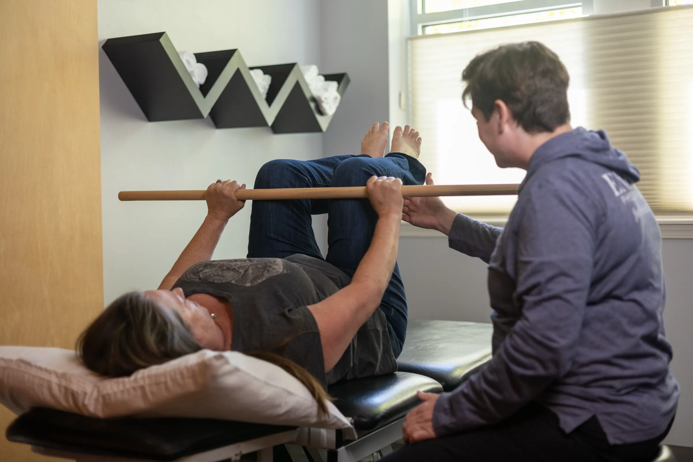 An Encore physical therapist guiding a patient through a shoulder mobility exercise with a dowel