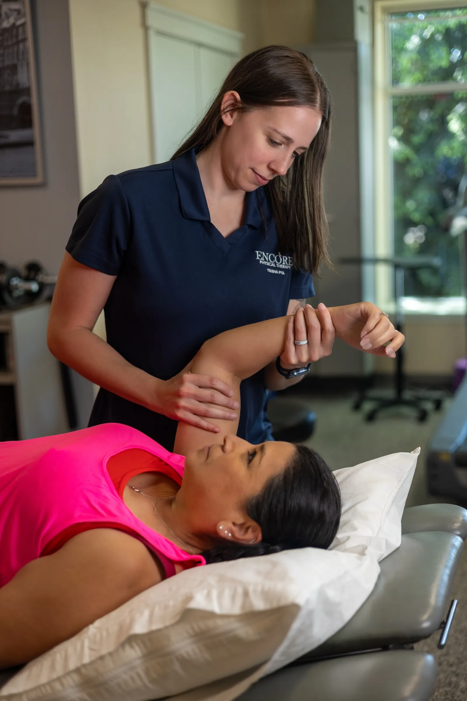 A physical therapist at Encore assessing a patient's shoulder on a treatment table